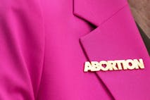 Photo: Christina House/2023 LA Times/Getty Images woman wears bright pink blazer featuring abortion pin with heart