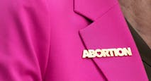 woman wears bright pink blazer featuring abortion pin with heart