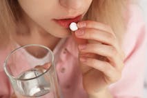 Young woman taking abortion pill on blurred background, closeup