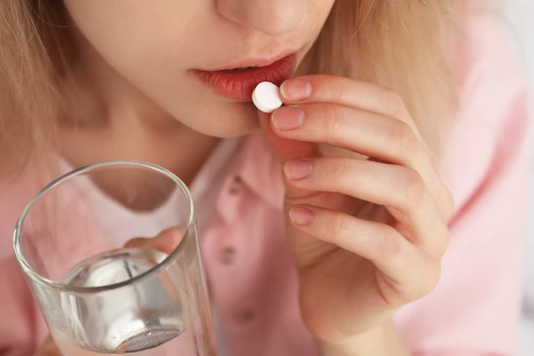Young woman taking abortion pill on blurred background, closeup