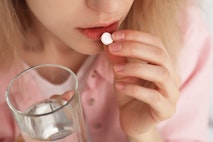 Young woman taking abortion pill on blurred background, closeup