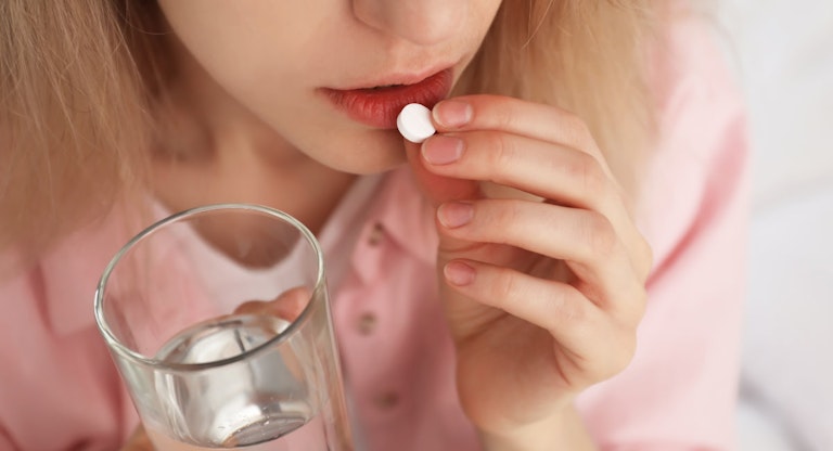 Young woman taking abortion pill on blurred background, closeup