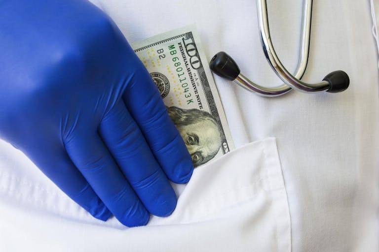 Doctor hides or lays down hundred dollar bill in pocket of white doctoral coat. Concept photo bribes, corruption in medicine, payment of medical care in private practice or public medicine, wages