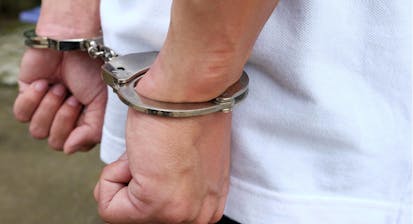 Close up of handcuffed hands held against a white shirt