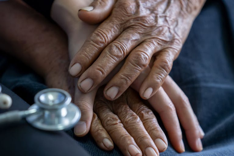 Close up of young nurse holding old man’s hands and encourage him.