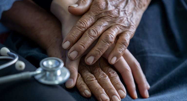 Close up of young nurse holding old man’s hands and encourage him.