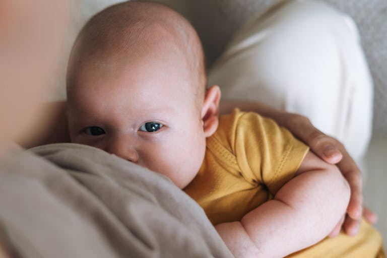 Young mother breastfeeding your 2-3 month baby boy lying on blanket at home