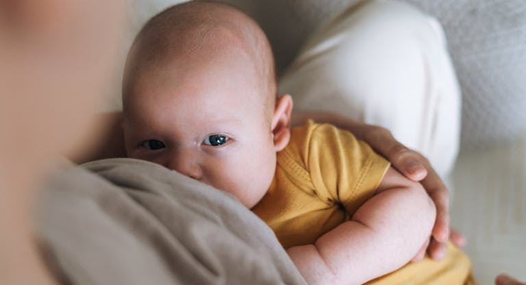 Young mother breastfeeding your 2-3 month baby boy lying on blanket at home