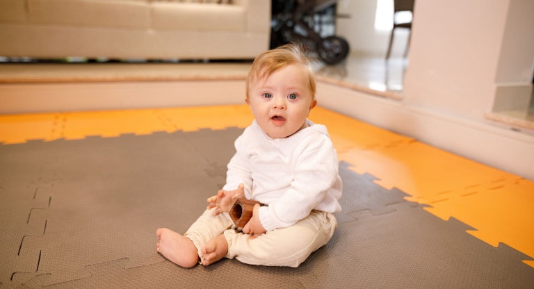Down syndrome baby sitting down on the living room