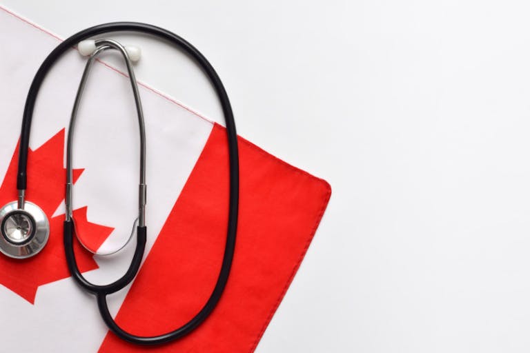 Canada healthcare concept, stethoscope on top of Canadian flag on white background with copy space