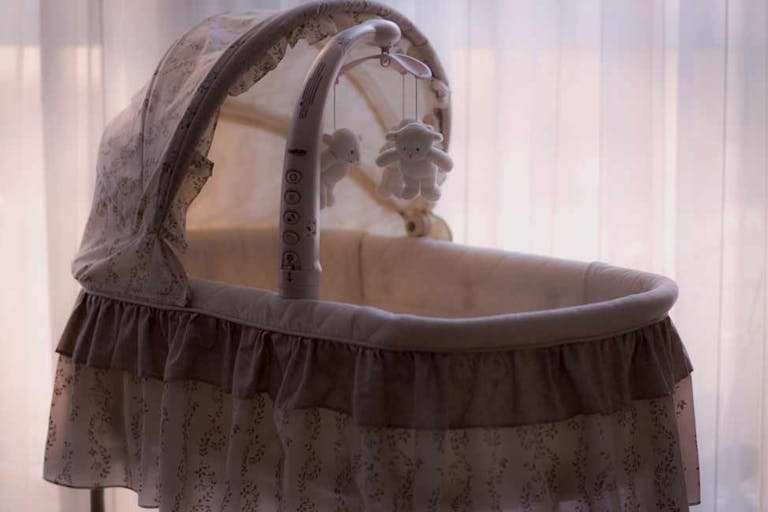 Photo via Unsplash A white bassinet sits empty in front of a window.