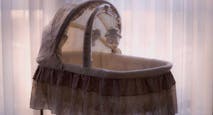 A white bassinet sits empty in front of a window.