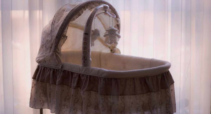 A white bassinet sits empty in front of a window.