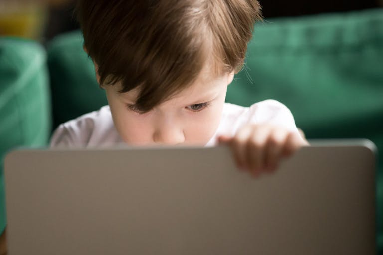 Curious kid boy secretly watching forbidden censored content on laptop