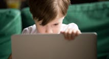 Curious kid boy secretly watching forbidden censored content on laptop