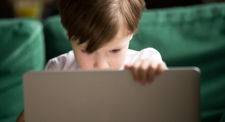 Curious kid boy secretly watching forbidden censored content on laptop
