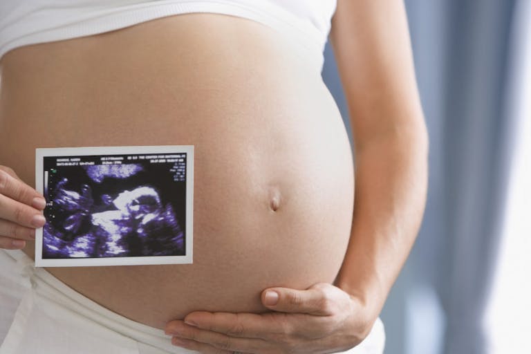 Pregnant Hispanic woman holding ultrasound printout