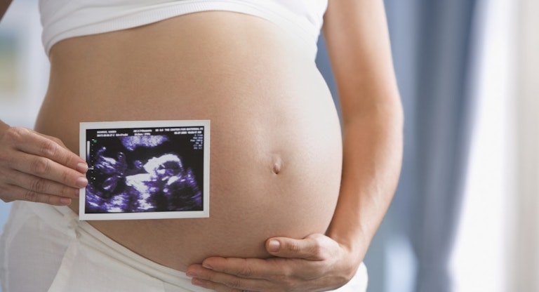Pregnant Hispanic woman holding ultrasound printout