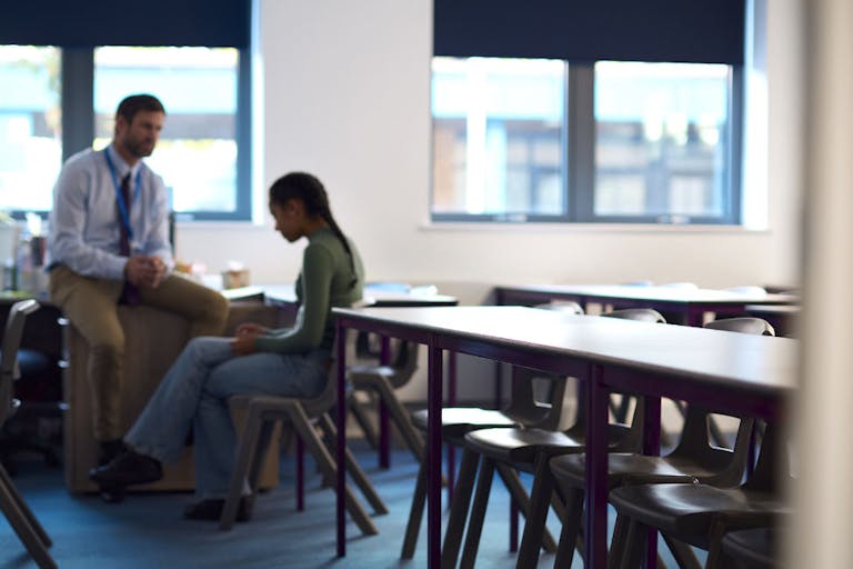 Secondary Or High School Teacher Sitting In Classroom With Unhappy Female Student After Lesson