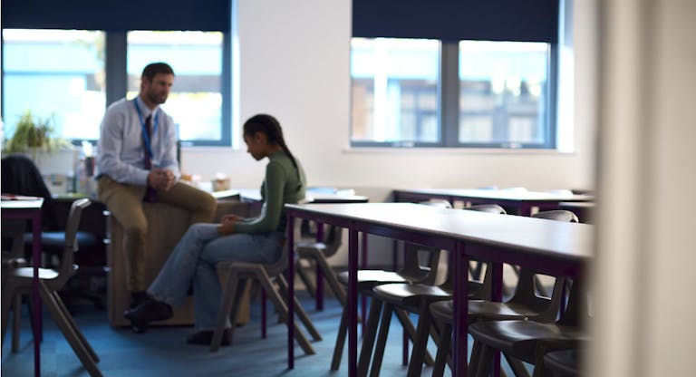 Secondary Or High School Teacher Sitting In Classroom With Unhappy Female Student After Lesson