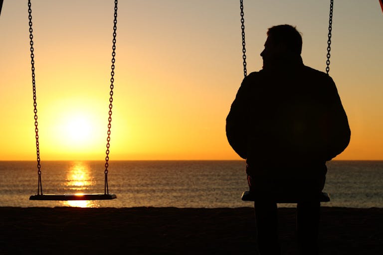 Man alone on a swing looking at empty seat