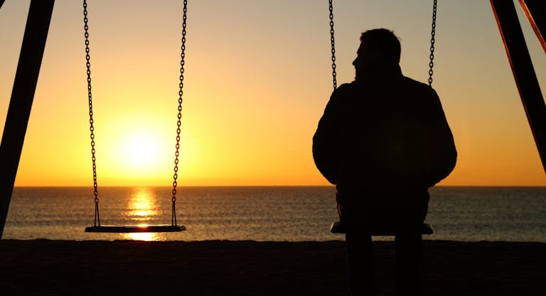 Man alone on a swing looking at empty seat