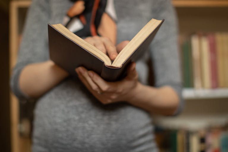 Beautiful young pregnant woman holding book in library