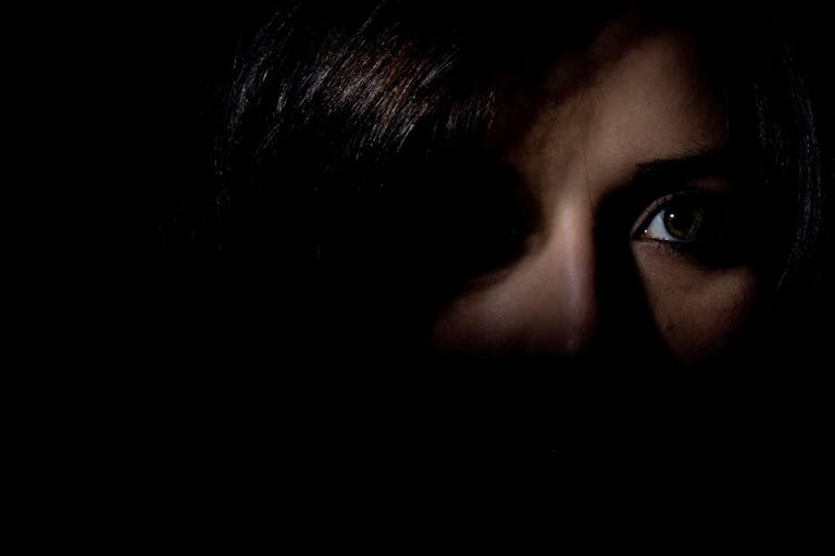 Woman stood in the dark showing half her face looking scared