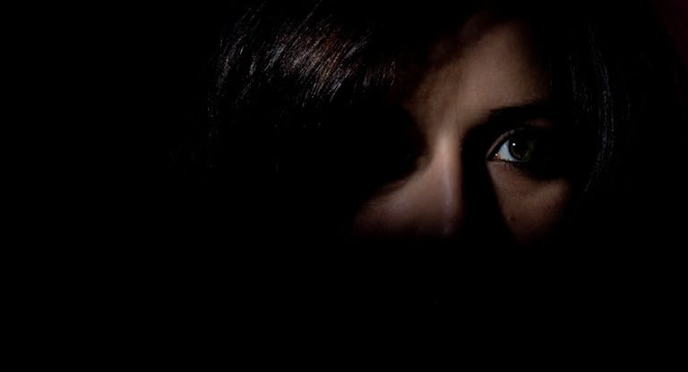 Woman stood in the dark showing half her face looking scared