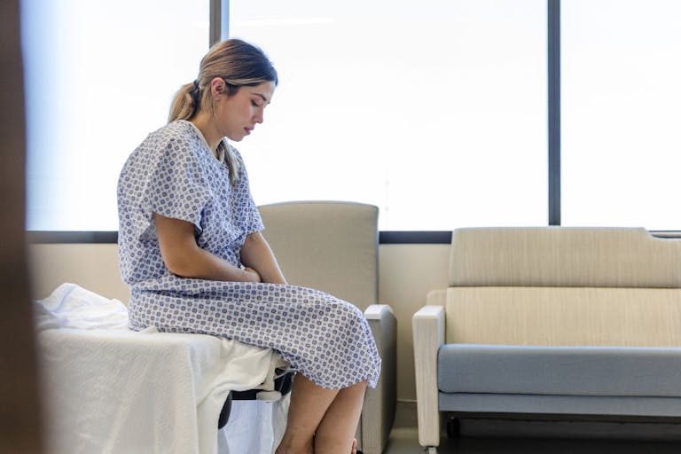 Anxious, sad, young woman wearing hospital gown looks down