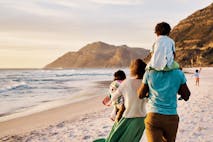 African parents with little kids bonding and strolling by ocean. Little children enjoying the outdoors during their summer holidays or vacation. Rear of a family walking on the beach with copy space