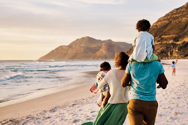 African parents with little kids bonding and strolling by ocean. Little children enjoying the outdoors during their summer holidays or vacation. Rear of a family walking on the beach with copy space