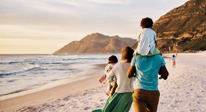 African parents with little kids bonding and strolling by ocean. Little children enjoying the outdoors during their summer holidays or vacation. Rear of a family walking on the beach with copy space