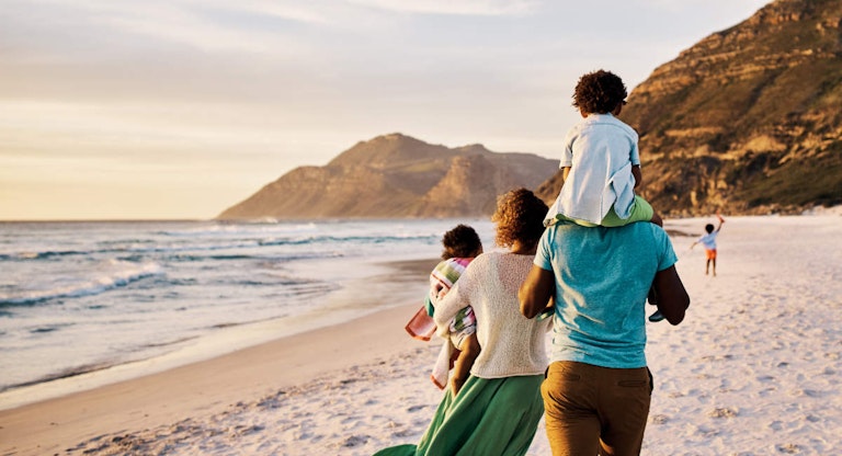 African parents with little kids bonding and strolling by ocean. Little children enjoying the outdoors during their summer holidays or vacation. Rear of a family walking on the beach with copy space