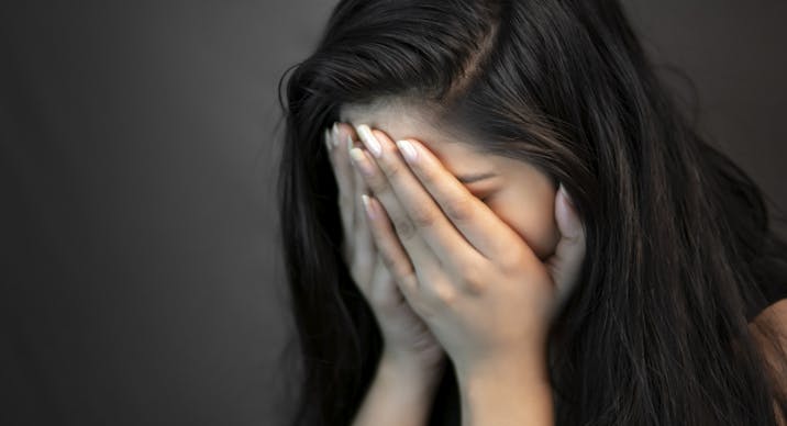 Portrait of stress young woman covering her face with hands and crying.
