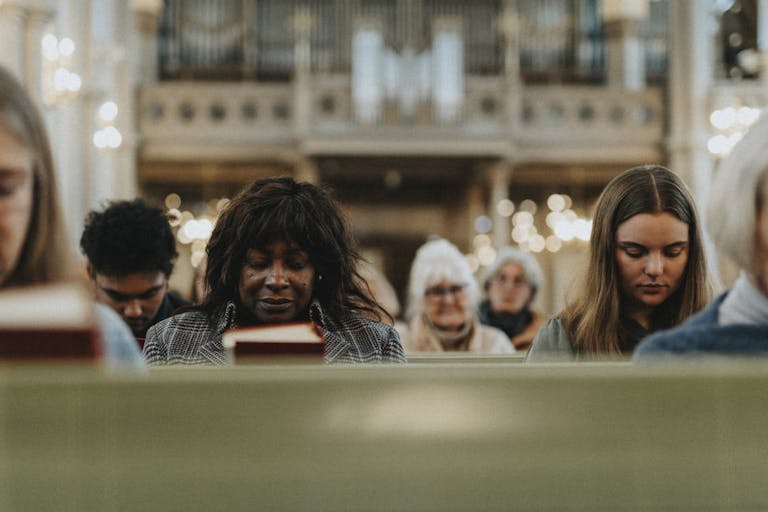 Group of male and female protestants praying with eyes closed while sitting at church