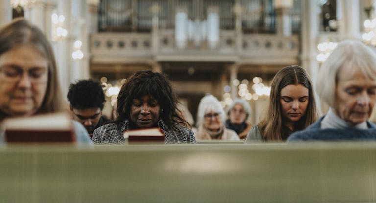 Group of male and female protestants praying with eyes closed while sitting at church