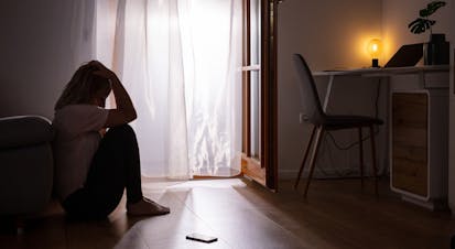 Side view full length shot of a sad depressed woman sitting on the floor and crying at home