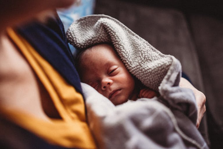 Newborn Baby is Held By Mother with Dramatic Window Light and Blankets