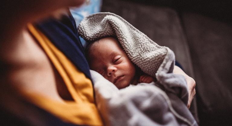 Newborn Baby is Held By Mother with Dramatic Window Light and Blankets