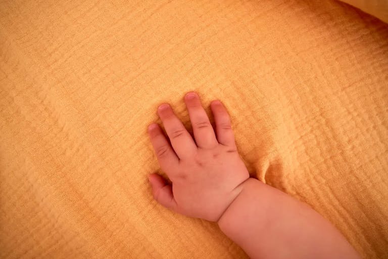 Baby’s hand on a yellow muslin swaddle.