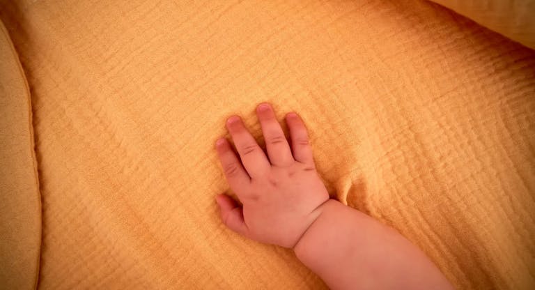 Baby’s hand on a yellow muslin swaddle.