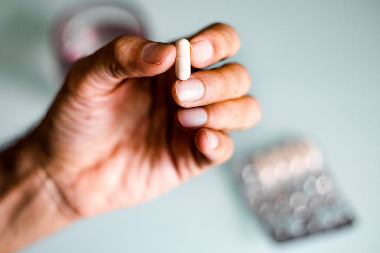 A man’s hand holding a capsule / pill
