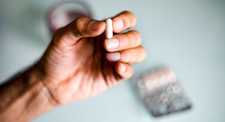 A man’s hand holding a capsule / pill