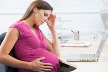 Pregnant woman at work with laptop looking stressed