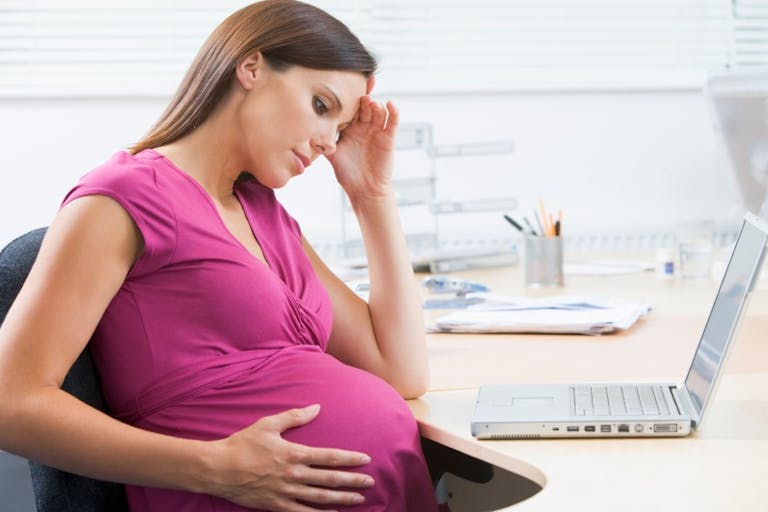 Pregnant woman at work with laptop looking stressed