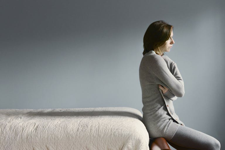 Sad Caucasian woman sitting on bed frame