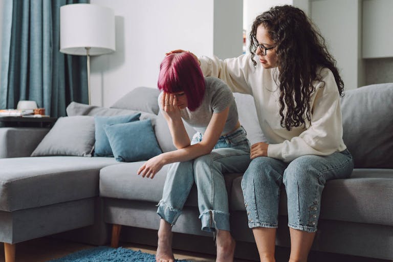 Adult curly haired woman consoling, stroking teen girl, sitting on a sofa. (Getty Images)