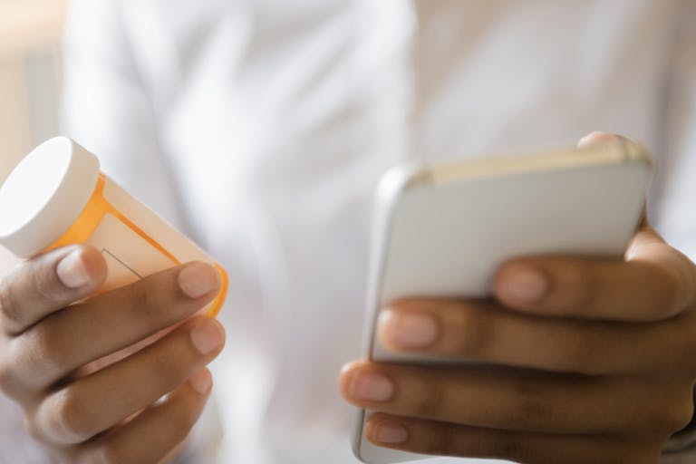 Hands of African American woman holding cell phone and pill bottle