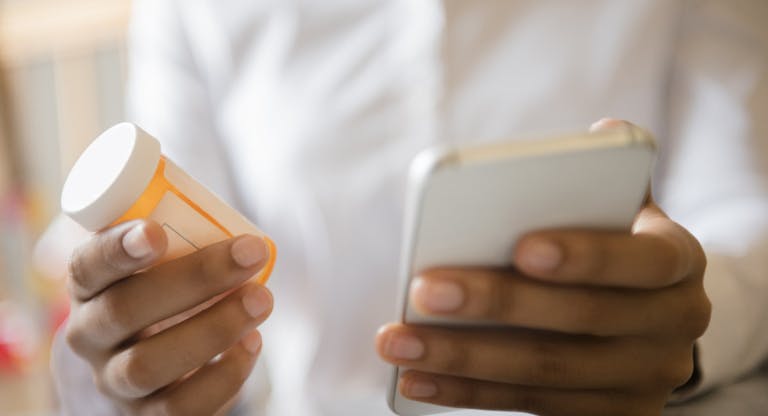 Hands of African American woman holding cell phone and pill bottle